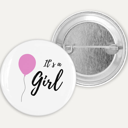 Button badge with 'It's a Girl' text and pink balloon on a white background